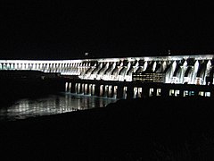 A gigantic concrete dam at night lit by powerful floodlights