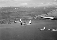 Black and white photo of four single-engined military monoplanes flying in formation near a coastline