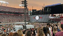 An Eras Tour stage in the middle of a filled stadium with a clock on screen behind it