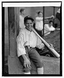 A batboy holding a baseball bat on his shoulder while sitting down