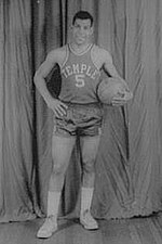 A man, wearing a jersey with a word "TEMPLE" and the number "5" written in the front, is holding a basketball while posing for a photo.