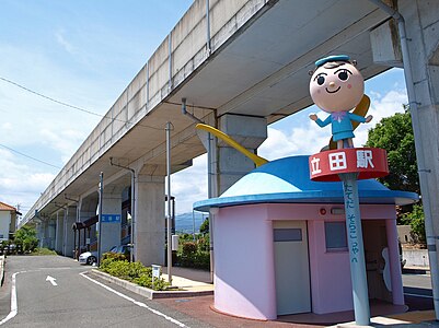 Tateda Station entrance. Note the propellers on the toilet building and the mascot character. The steps leading to the platform are in the background.