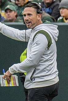 LaFleur on the sideline wearing a headset and holding a playsheet