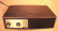 A black box with wood veneer sides. On the front is a silver area containing two knobs.