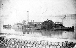 Black and white photo shows a paddle wheel river boat with two smokestacks, a sloping casemate, and gunports.