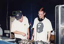 Two men stand behind a set of turntables in 1997.