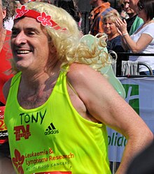 Headshot of man with blonde wig in fluorescent yellow running top.