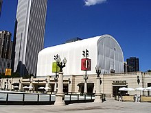 A large white tent sits on the roof of a cafe building set in front of a skyscraper and blue sky.