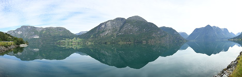 Panorama of Oppstrynsvatnet from the south side of the lake. The mountains Oppigardshyrna and Lægdekulen are visible in the center of the image. The village of Flo is located to the left of the two mountains. The mountain Hjellehyrna at the east end of the lake is visible on the right of the image