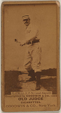A sepia-toned image of a man wearing an old-style white baseball uniform and cap throwing a baseball