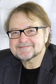 head and shoulders of Urrea with light brown hair, black glasses, with a goatee