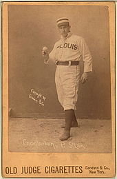 A baseball player is standing, facing the camera, holding a baseball.