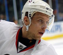 Head view of a hockey player in a white uniform and helmet as he stares intently into the distance.