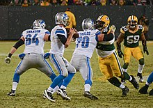 A photo of Matthew Stafford holding the football after it has been snapped. Packers defenders are in the background.