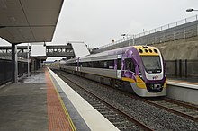 Silver, purple and yellow three-carriage train waiting at a railway station.