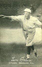 A man in an old-style baseball uniform, seemingly in the act of pitching a baseball