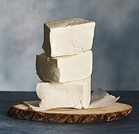 Three thick white blocks of arabieh/baida cheese are stacked atop a wooden serving board.