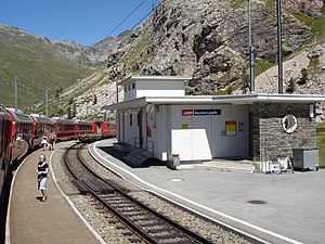 Red train parked at station; the station building is single-story with a flat roof