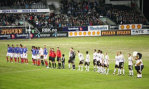 A line of footballers, in blue and white, respectively, at a large stadium