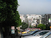 City landscape, with gray skies above the windshields of parked cars overlooking the distinctive buildings of San Francisco.