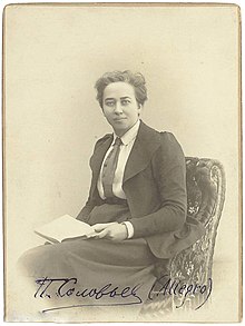 Sepia portrait of a short-haired woman wearing a jacket and long skirt, seated with a book in her lap.