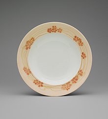 A white shallow bowl with a border of light orange with darker orange flowers and gold streaks.