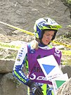 A woman in her mid-20s wearing a blue and yellow open-face crash helmet and motorcross overalls