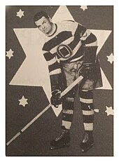 Black and white image of a hockey player wearing a horizontal-striped jersey, wearing hockey equipment, posing with a hockey stick