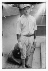 A man in an old-stye baseball uniform stands in a dugout