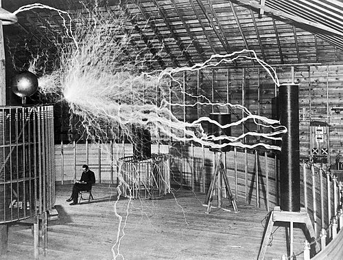 Photograph of Nikola Tesla seated next to a high-voltage generator
