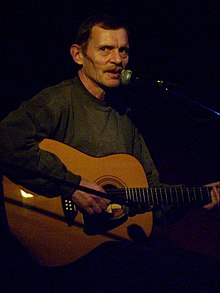 Jiří Schmitzer seated, playing guitar, looking to the right at camera