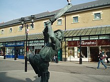 Statue of a man holding a cricket bat, with some shop fronts in the background.