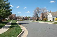 A meandering suburban street. On both sides there are rows of houses with lawns in front of them.