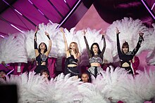 Blackpink with their hands raised, surrounded by feathers
