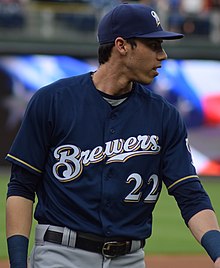 A man wearing a navy blue Brewers jersey, gray pants, and a navy blue cap on a baseball field