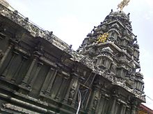 A black granite construction of a temple tower with a metal disc and miniature at the top