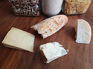 A mixture of cheeses on a wooden cutting board, comprising blue, cheddar and goat gouda, with a loaf of bread