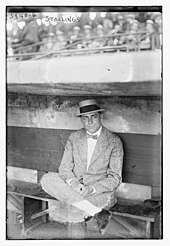 Man in a suit and hat sitting in a baseball dugout