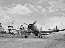 Black and white photo of a single-engined military monoplane on a runway. A man is seated on each of the plane's wings.