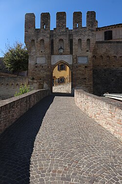A pointed arch castle entrance with crenellations at the top. The brick is grey-red.