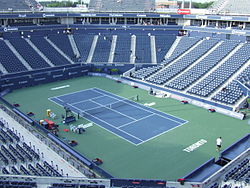 View of tennis court surrounded by blue stands of seating in stadium