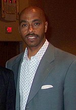 A man, wearing a gray suit and white shirt, is standing and posing for a photo.