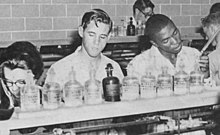 Students in a laboratory standing in front of a counter with bottles on it