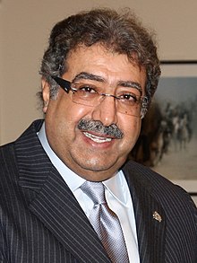 A photo of Prince Faisal bin Abdullah, a middle aged man with glasses, suit and tie. He appears happy.