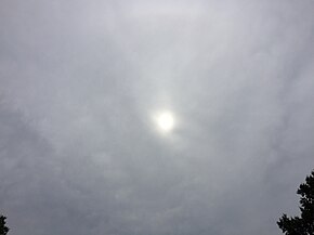 The sun shines diumly through a largely-featureless gray altostratus cloud.