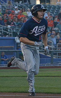 A man in a navy blue baseball jersey and batting helmet and gray pants