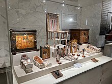 A chair, two boxes, and various ushabti in a tiered display case