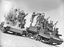 Soldiers standing on two mechanised vehicles in the desert