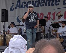 A man wearing a dark blue shirt and jeans is holding a microphone on his right hand.
