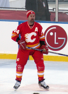 A hockey player in a red uniform with yellow and white trim and matching toque. The logo on the chest is a white stylized "flaming C"